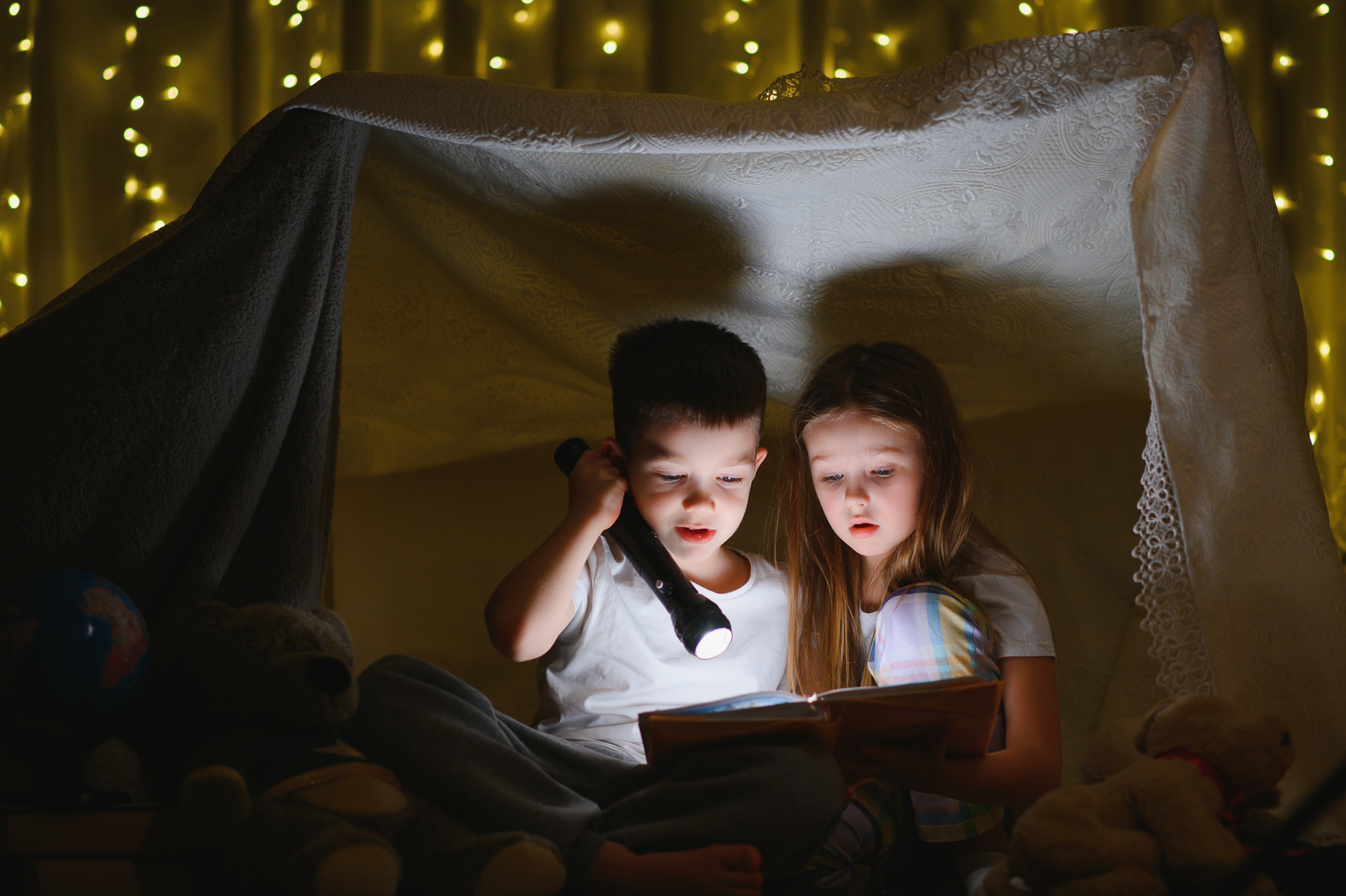 boy and girl reading by flashlight in blanket fort